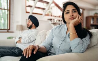 Sad young Indian woman avoiding talking to husband while sitting on sofa