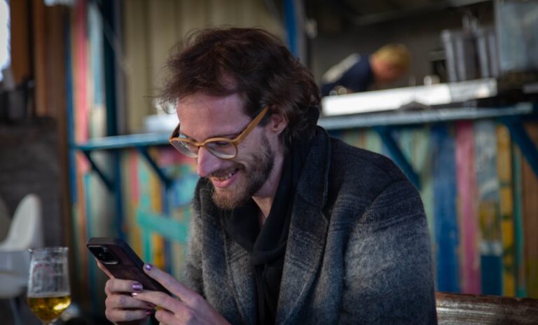 Man using a smartphone while seated in a bar, illustrating online dating and Badoo profile strategy