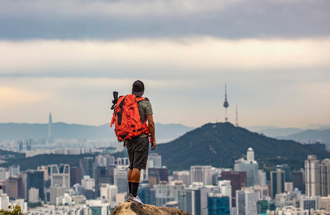 Man with backpack overlooking a city from a high viewpoint, illustrating independence, travel and long-term life planning